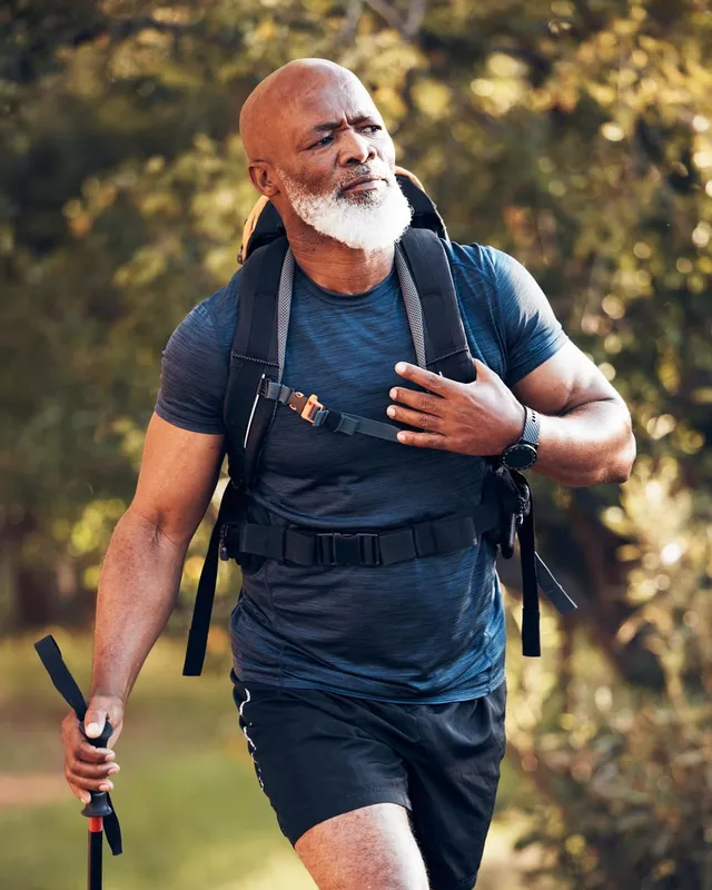 An older hiker on a wooded trail with a backpack and trekking pole